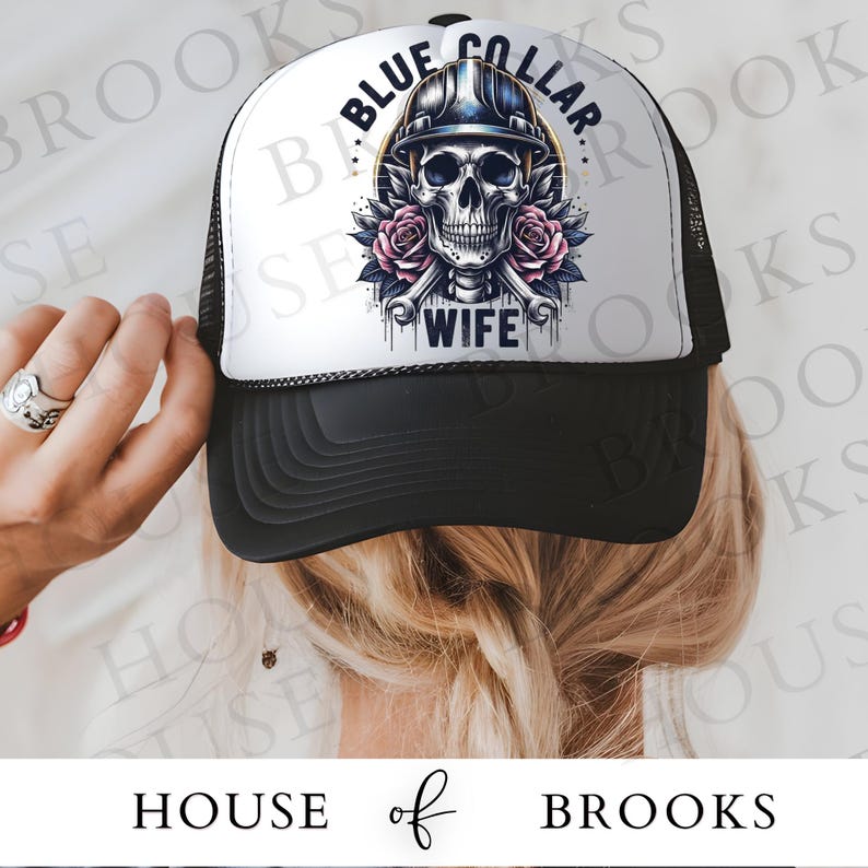 May include: A white trucker hat with a black mesh back. The front of the hat features a skull wearing a hard hat and holding two wrenches. The text "Blue Collar Wife" is printed below the skull.