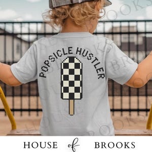 May include: A light gray t-shirt with the words "POPSICLE HUSTLER" arched above a pixelated popsicle design in black and white checkered pattern. The popsicle has a brown stick. The brand name "HOUSE of BROOKS" is at the bottom.