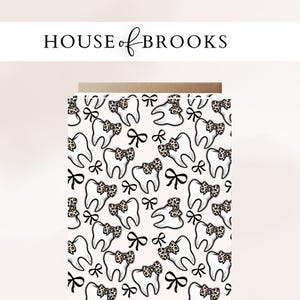 May include: Card with a repeating pattern of cartoon teeth wearing leopard print bows and black bows on a light pink background. The text "HOUSE of BROOKS" is at the top in black.