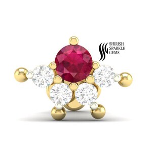 May include: A gold-colored stud earring with a starburst design. The center features a round, deep red gemstone, surrounded by five white, sparkling gemstones. The earring has a post and backing.