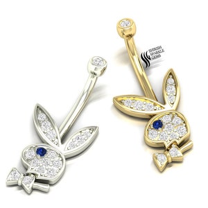 May include: Two belly button rings, one silver and one gold, each featuring a bunny design. The bunnies are encrusted with small, sparkling white stones and a single blue stone for the eye. The gold ring has a curved bar.
