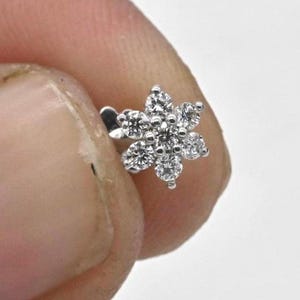 May include: A silver flower-shaped nose ring with clear cubic zirconia stones.