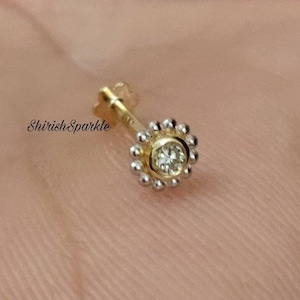 May include: A gold nose ring with a small, clear gemstone set in a circle of tiny beads.
