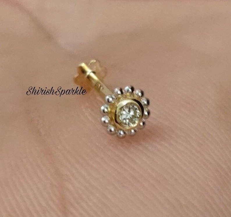 May include: A gold nose ring with a small, clear gemstone set in a circle of tiny beads.