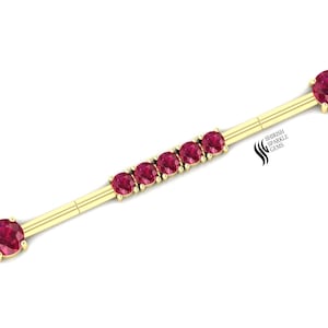 Puede incluir: Barbell de oro con seis piedras preciosas rojas. El barbell es una joya de piercing corporal.  "Shirish Sparkle Gems" está impreso en el barbell.