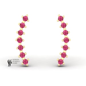 May include: A pair of gold-colored climber earrings. Each earring features a curved design with a series of vibrant pink gemstones. The earrings are set against a white background. The logo "SHIRISH SPARKLE GEMS" is visible.