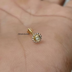 May include: A gold nose ring with a small, clear gemstone set in a circle of small beads.