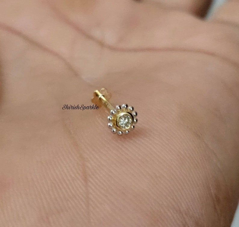 May include: A gold nose ring with a small, clear gemstone set in a circle of small beads.
