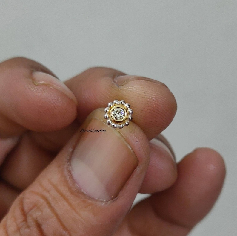 May include: A gold nose ring with a clear gemstone in the center and a circle of small gold beads around the gemstone.