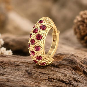 Peut inclure: Une créole en or présentant un motif en treillis avec de petites pierres précieuses rondes rouge foncé serties dans chaque ouverture en forme de losange. La surface métallique présente un design perlé texturé sur les bords.