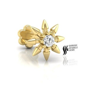 May include: A gold nose ring with a star-shaped design and a single diamond in the center. The star has eight points, each ending in a small spike.