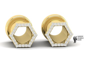 May include: Two gold-colored ear gauges with a hexagonal design. The hexagon is outlined with small, clear gemstones. The jewelry has a polished finish and is set against a white background. The brand name "SHIRISH SPARKLE GEMS" is visible.
