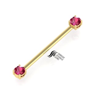 Op de afbeelding: Gouden barbell met twee rode edelstenen. De barbell is een lichaamssieraden.