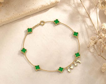 Könnte beinhalten: Ein goldenes Kettenarmband mit sechs grünen kleeblattförmigen Anhängern und drei kleinen hängenden Anhängern in Form eines Diamanten, eines Herzens, eines Sterns und einer Mondsichel. Das Armband besteht aus einer feinen Gliederkette und einem runden Verschluss.