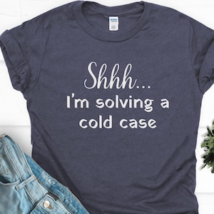 May include: A navy blue t-shirt with the text "Shhh... I'm solving a cold case" printed in white.