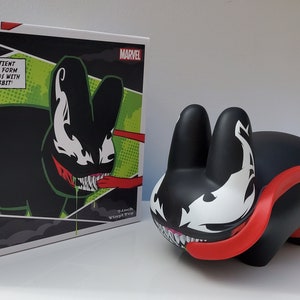 May include: A black and white Venom Labbit figure with red accents. The figure is a stylized cartoon version of the Marvel Comics character Venom. The figure is packaged in a box with a comic book style design featuring the character Venom.