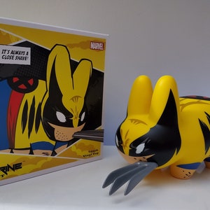 May include: A yellow, black, and blue Wolverine Labbit vinyl toy with a comic book style design. The toy is holding a pair of silver claws. The toy is packaged in a box with the words "Wolverine Labbit" and "It's always a close shave!" printed on it.