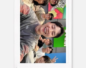 May include: A polaroid-style photograph featuring a group of smiling individuals. The subjects, with diverse appearances, are captured in a close-up shot. The background includes green and blue hues, adding a vibrant contrast to the image.