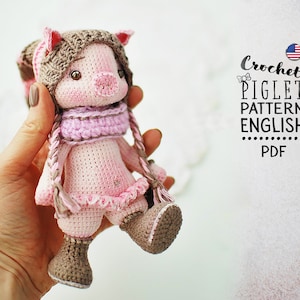 Könnte beinhalten: Häkelanleitung für ein Ferkel auf Englisch, PDF-Format. Eine rosa gehäkelte Ferkelpuppe mit braunem Hut, rosa Schal und rosa Stiefeln.