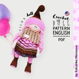 Puede incluir: Muñeca Tilda hecha a mano con una combinación de colores rosa y marrón. La muñeca tiene un sombrero largo y puntiagudo, pelo rosa y una bufanda de ganchillo. La imagen también incluye el texto "Crochet Doll Pattern English PDF".