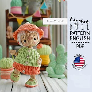 Può includere: Una bambola all'uncinetto con un maglione verde e una gonna arancione, con cappello e scarpe abbinati. La bambola ha i capelli bianchi e si trova di fronte a una mensola con oggetti decorativi. Il testo dice "Crochet Doll Pattern English PDF".