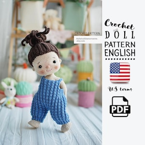 Può includere: Una bambola all'uncinetto fatta a mano, con capelli castani e una tuta blu. La bambola ha un viso dettagliato con un'espressione neutra. L'immagine include il testo "Crochet Doll Pattern English" e un'icona della bandiera americana.