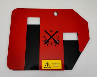 May include: Red metal plate with black cutouts and a warning sign. The sign reads "Pedal release before driving, remove!" The plate also has a compass rose with the letters N, S, E, and W.