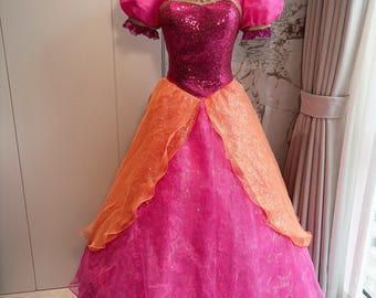 Könnte beinhalten: Ein bodenlanges Kleid mit einem magentafarbenen Paillettenoberteil, herzförmigem Ausschnitt und kurzen Puffärmeln. Der Rock besteht aus Lagen rosafarbenem Stoff mit Blumenmuster und einem orangefarbenen Organza-Überrock mit Goldborte.