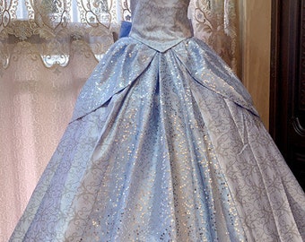 May include: A light blue ball gown with a silver glitter pattern. The dress has a sweetheart neckline and short puffed sleeves. The skirt is full and flowing.