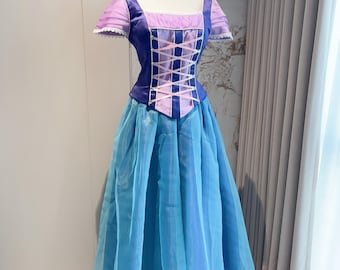 Könnte beinhalten: Prinzessinnenkleid auf einer Schaufensterpuppe. Das Oberteil ist tiefblau mit einem rosa Korsettmuster, die Ärmel sind lavendelfarben. Der Rock ist fließend, blau und mehrlagig, mit dunklerem blauem Saum. Geeignet für Kostüm oder besondere Anlässe.