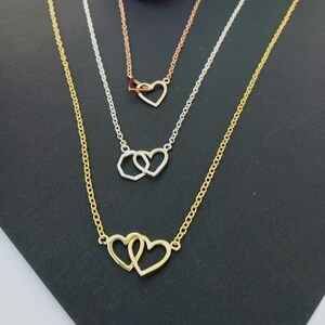 May include: Three necklaces with heart pendants. The top necklace is rose gold, the middle one is silver, and the bottom one is gold. Each necklace has a delicate chain. The hearts are different designs, including interlocking and open hearts.