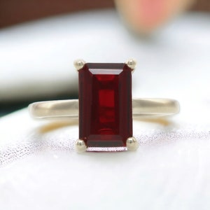 Op de afbeelding: Een ring met een grote, rechthoekige, donkerrode edelsteen gezet in een zilveren band.