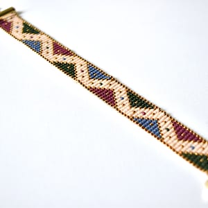 K&ouml;nnte beinhalten: Ein Armband aus Perlen mit einem geometrischen Muster in Rosa-, Blau-, Gr&uuml;n- und Goldt&ouml;nen. Das Armband hat einen goldenen Verschluss.