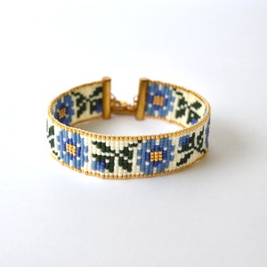 May include: A white beaded bracelet with a blue floral pattern and gold clasps.