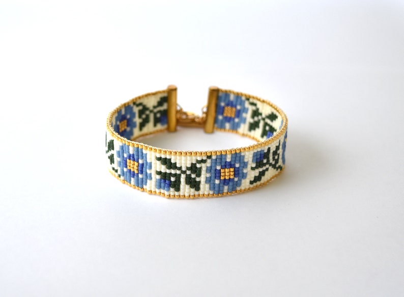 May include: A white beaded bracelet with a blue floral pattern and gold clasps.