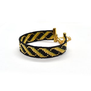 May include: A black and gold beaded bracelet with a geometric pattern. The bracelet has a gold clasp and chain.
