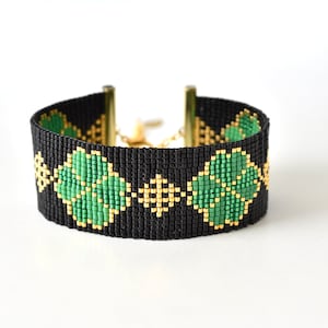 Könnte beinhalten: Ein schwarzes Perlenarmband mit einem goldenen Kettenverschluss und grünen und goldenen geometrischen Mustern.