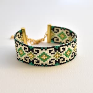 May include: A green, white, and black beaded bracelet with a geometric pattern. The bracelet has gold-toned clasps.