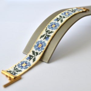 May include: A white beaded bracelet with a blue floral pattern and gold clasp.