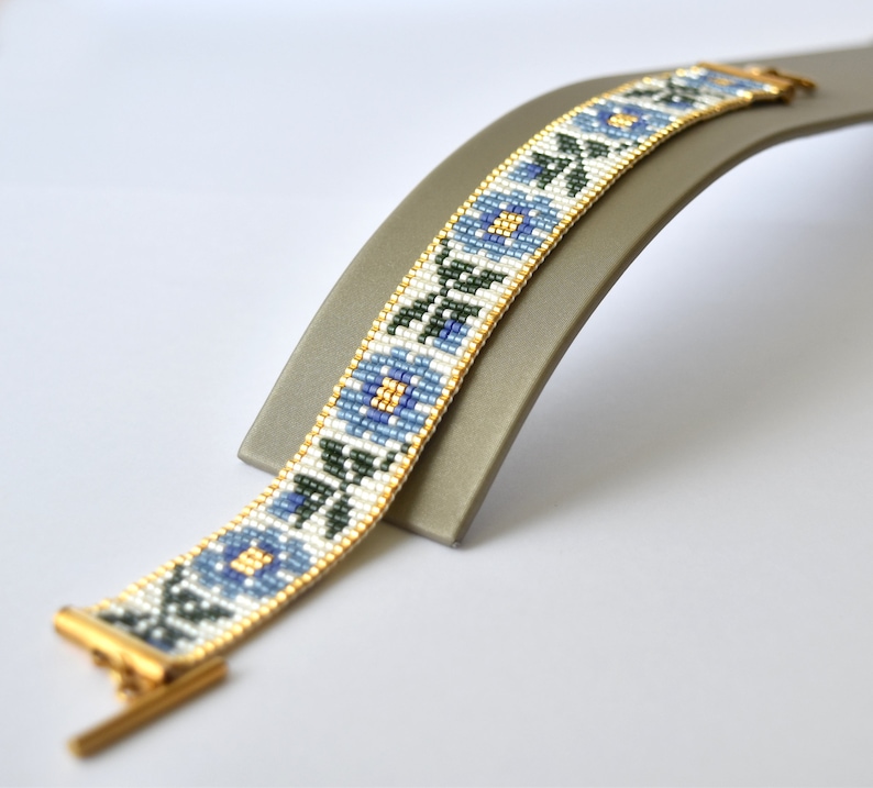 May include: A white beaded bracelet with a blue floral pattern and gold clasp.