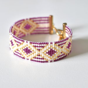 May include: A beaded bracelet with a geometric pattern in white, gold, and purple.