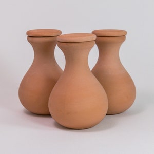 Peut inclure: Trois récipients en terre cuite avec des corps arrondis, des cols étroits et des couvercles circulaires plats. Chaque contenant présente une finition mate brun terreux avec une texture lisse, disposés en groupe pour montrer leur forme.