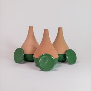 Peut inclure: Trois vases en terre cuite avec une base verte et des couvercles circulaires verts assortis. Les vases ont une forme de goutte d'eau et sont disposés sur un fond blanc. Le design est minimaliste et moderne.