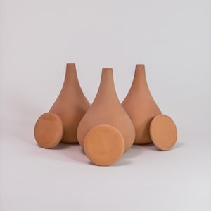 Peut inclure: Trois vases en céramique de couleur terre cuite avec un fond arrondi et une ouverture étroite en haut. Chaque vase est associé à un couvercle en céramique de couleur terre cuite assorti.