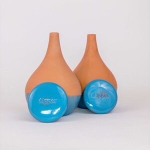 Peut inclure: Deux vases en terre cuite en forme de goutte d'eau avec une base bleue, accompagnés de deux objets ronds bleus assortis. Le mot "Alppos" est estampé sur les objets bleus. Les vases ont une finition lisse et mate.