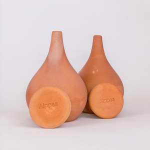 Peut inclure: Deux vases en forme de goutte d'eau de couleur terre cuite avec des cols étroits et deux dessous de verre ronds. Les dessous de verre et les vases portent le mot "Alppos". Le fond est blanc uni.
