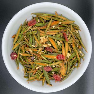 Puede incluir: Un bol blanco lleno de una mezcla de agujas de pino verdes y naranjas, arándanos secos y una cobertura desmenuzable de color marrón claro.