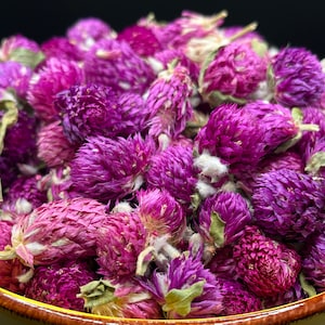 May include: A bowl filled with dried purple globe amaranth flowers. The flowers are a vibrant purple color and have a delicate, feathery texture.