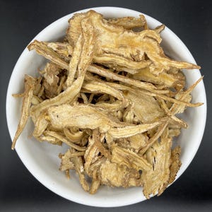 May include: A white bowl filled with dried, light brown, root pieces. The pieces are thin and have a slightly rough texture.