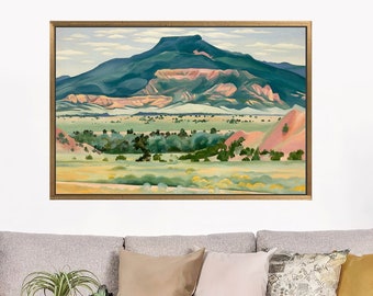 May include: A gray sofa with a variety of throw pillows, a throw blanket, and a small wooden table with two vases and a plant. The sofa is in front of a white wall with a framed landscape painting above it. A green plant is in a black pot on the right side of the image.